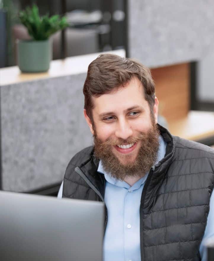 Mann mit Bart und Weste arbeitet bei FLEX Capital an einem Computer.